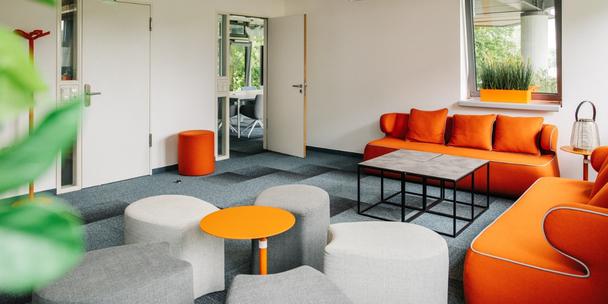 Kreative Lounge mit Blick auf den See. In Orange- und Grautönen gehalten. Durch die offene Tür können Sie einen anderen Raum sehen, der dazu gehört.